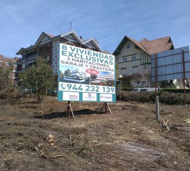 Letrero en medio de un terreno con varias casas construidas al fondo anunciando casas en venta y teléfono de contacto