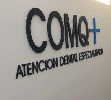 Cartel de logo corporativo de la empresa COMQ+ atención dental especializada sobre pared